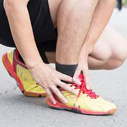 cropped image of a runner in red and yellow shoes having ankle pain