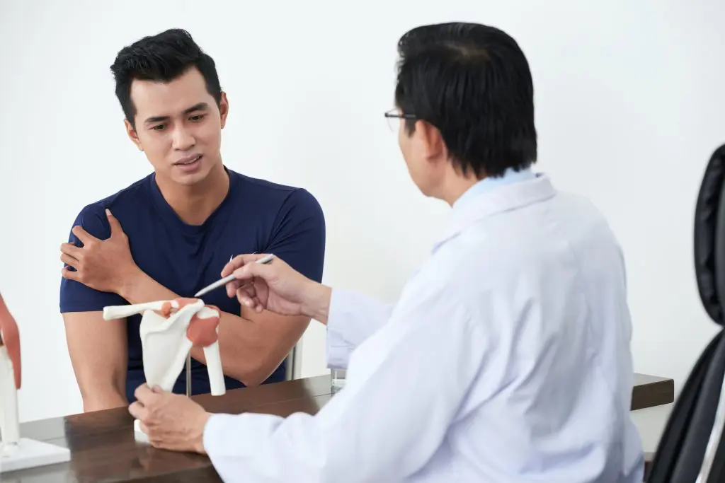 young male patient speaking to his chiropractor about his shoulder pain