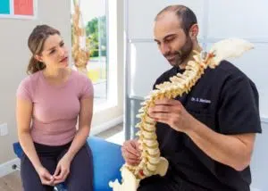 A chiropractor holding a model of a spine and explaining it to the female patient