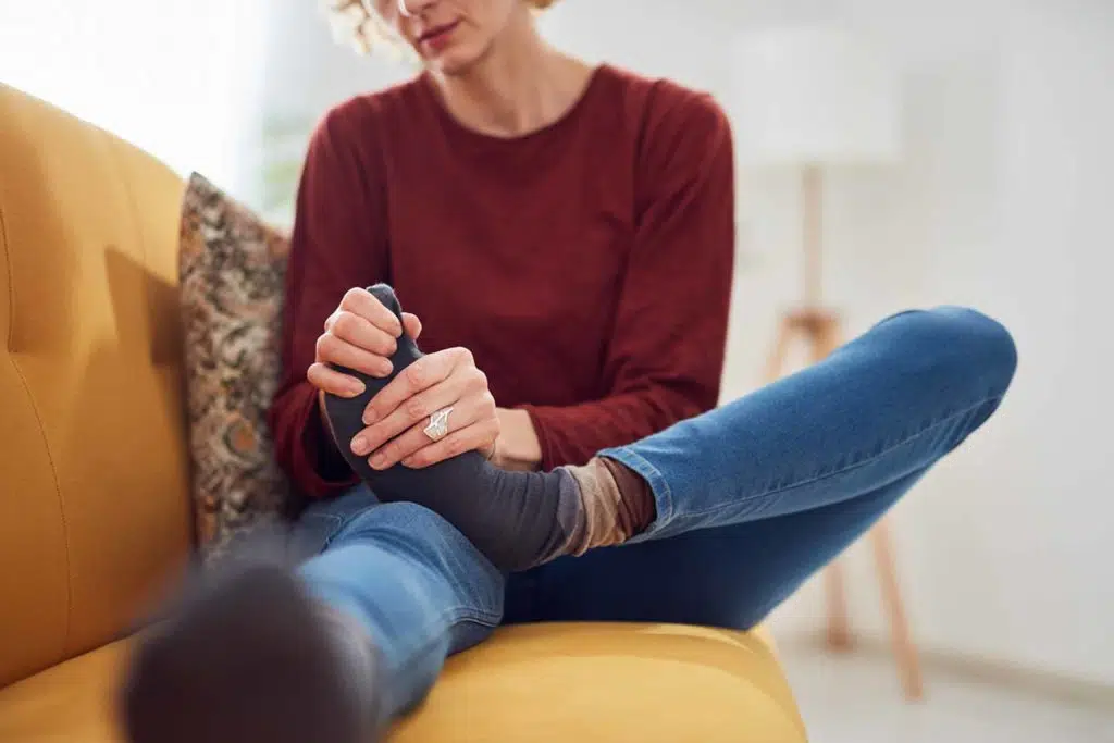 Woman with feet intense pain sitting on a couch at home.