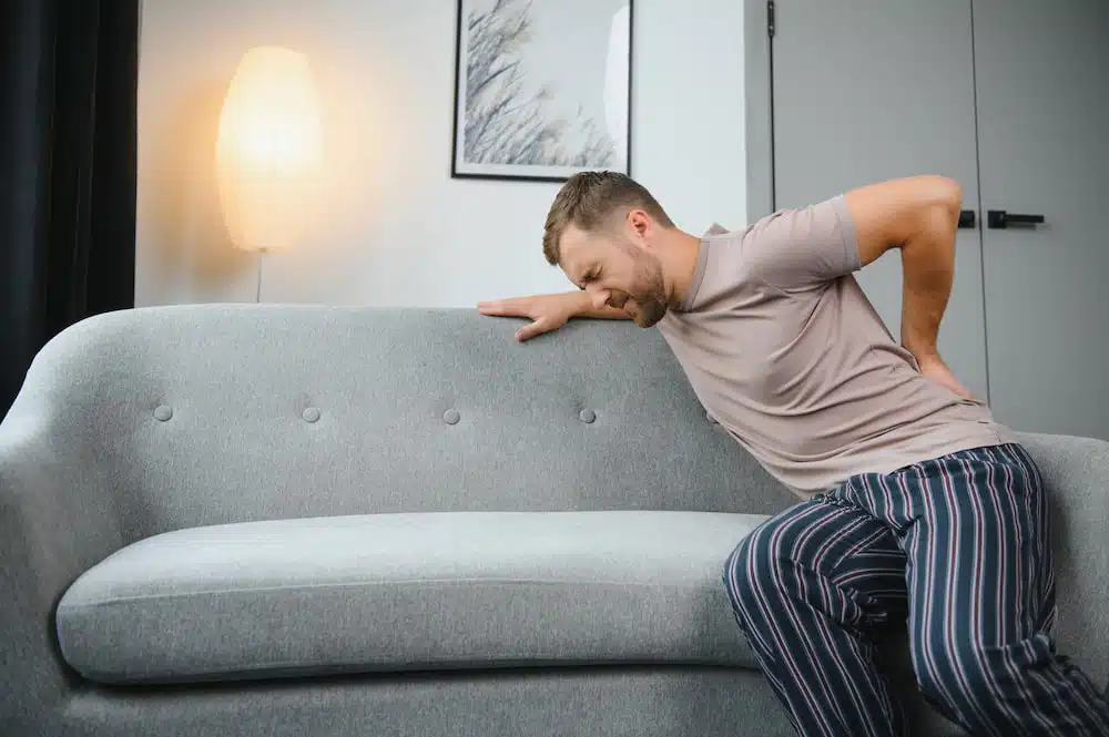 man sitting on the couch experiencing back pain from sciatica nerve problems